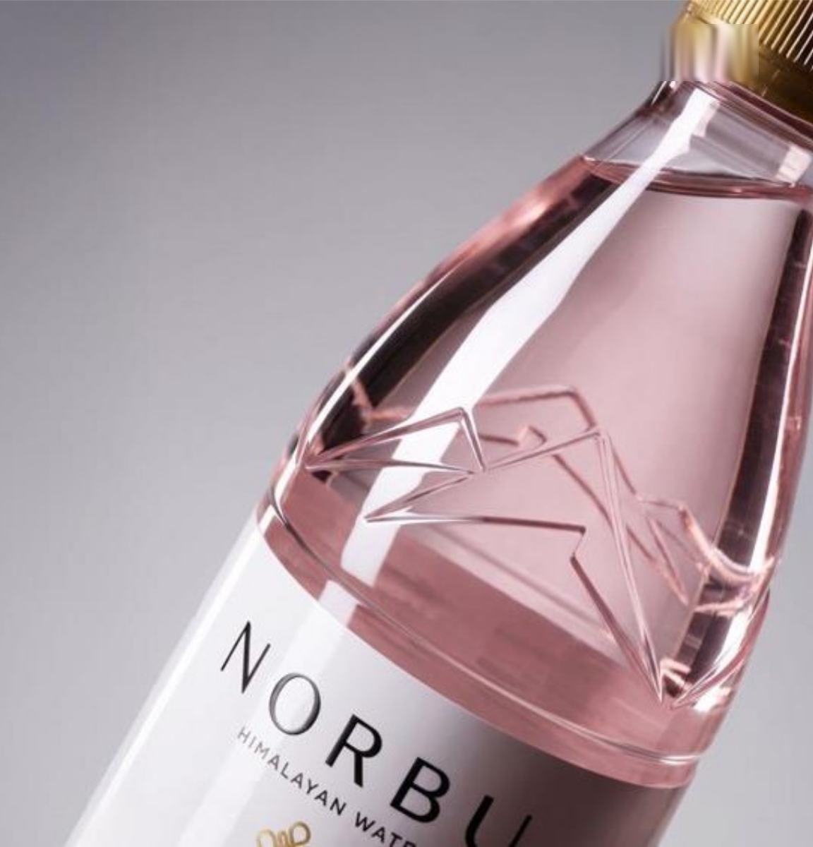 A blush-glass NORBU bottle with a faceted, sculpted body and gold cap.