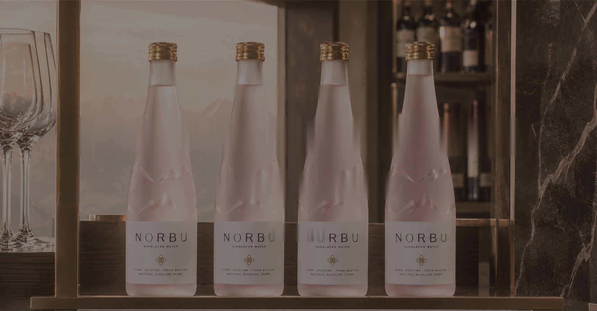 Four NORBU bottles lined along a lit bar shelf beside glassware.